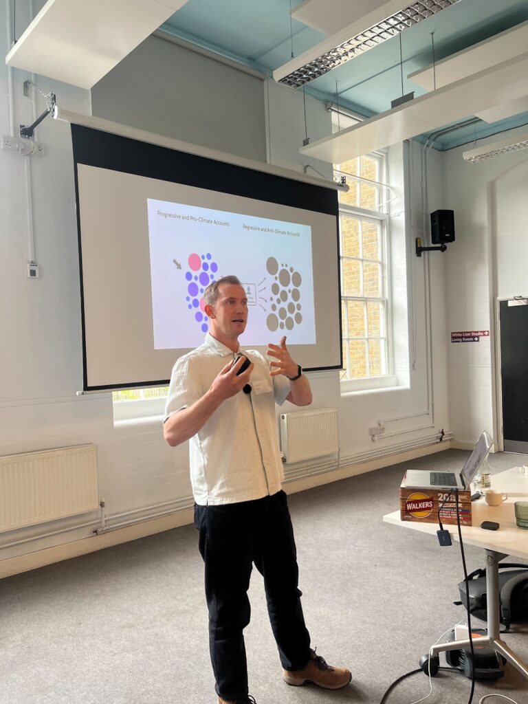 Speaker presenting in front of a projected network diagram comparing progressive and anti-climate online communities, gesturing while presenting research and strategy insights to workshop participants