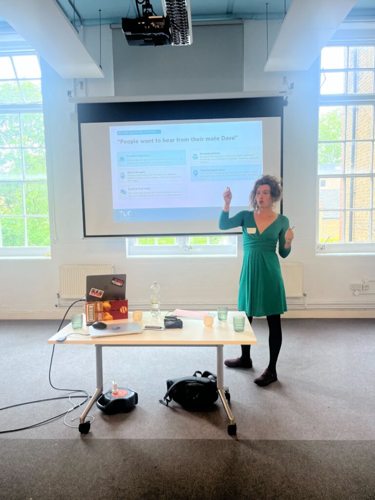 Speaker delivering a presentation on trusted messengers and grassroots climate campaigning communications, standing in front of projected slides about community voices and public trust during a workshop session