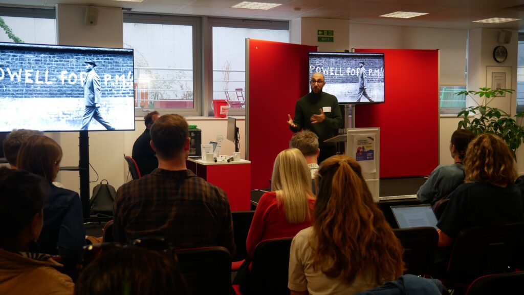 Speaker presents on the history of the radical right in the UK, with an archive photograph of "Powell for PM" graffiti on screen