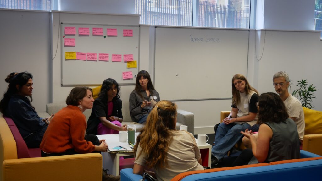 Campaigners in a small group discussion on strategies to counter the radical right, with session notes on the whiteboard behind. Everyone looks at one participant as they speak.
